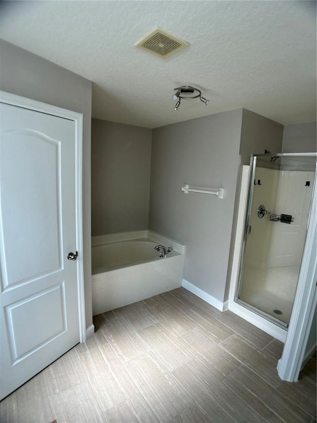 bathroom with a shower stall, a bath, a textured ceiling, and baseboards
