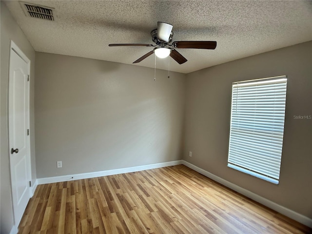 spare room featuring light wood-type flooring, a ceiling fan, baseboards, and a textured ceiling