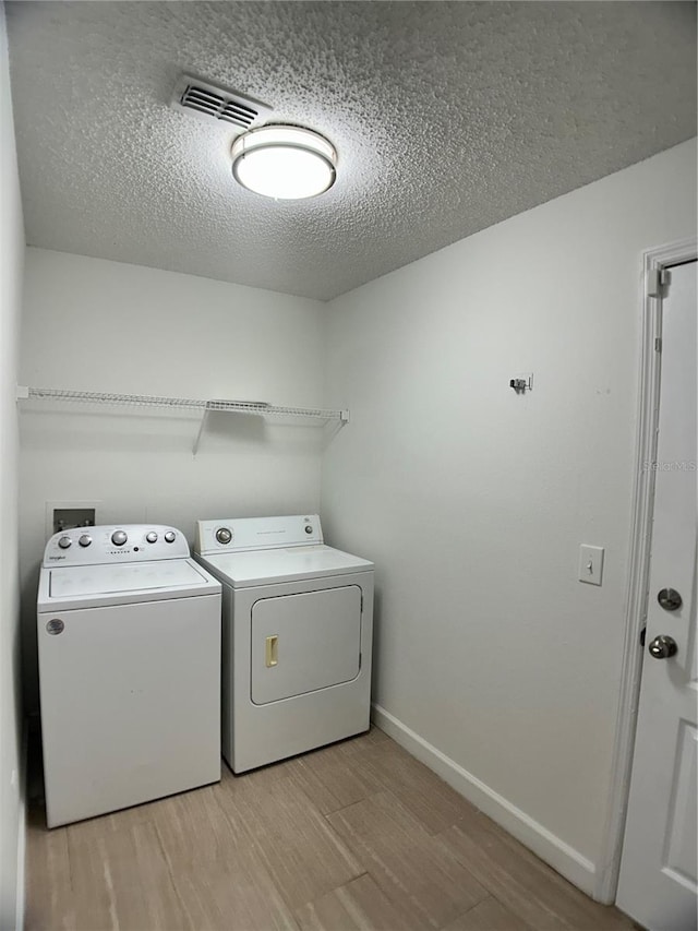 laundry area featuring independent washer and dryer, light wood finished floors, a textured ceiling, and baseboards