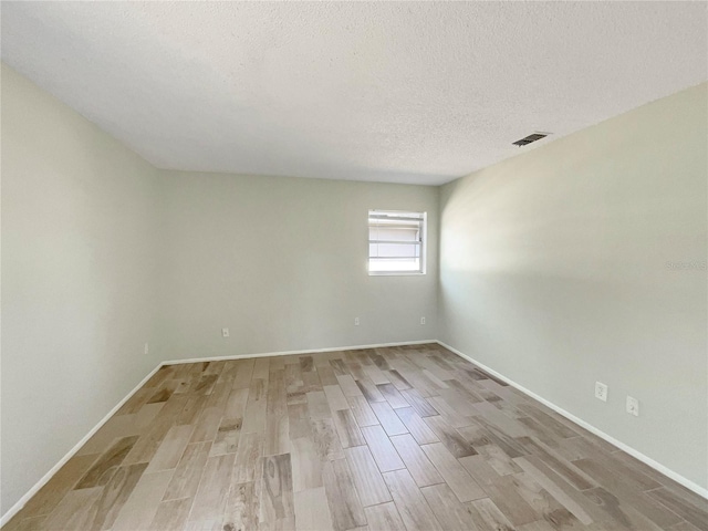 spare room featuring light wood-style floors, baseboards, and a textured ceiling