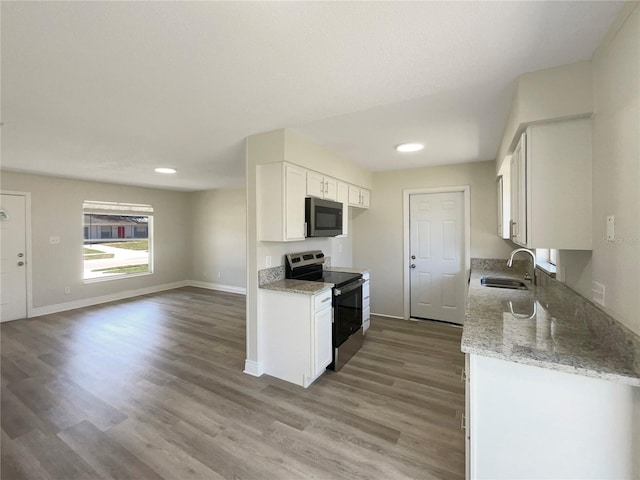 kitchen with appliances with stainless steel finishes, a sink, light stone countertops, white cabinets, and light wood-style floors