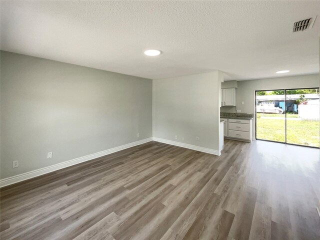 unfurnished living room featuring dark wood-style flooring, baseboards, and a textured ceiling