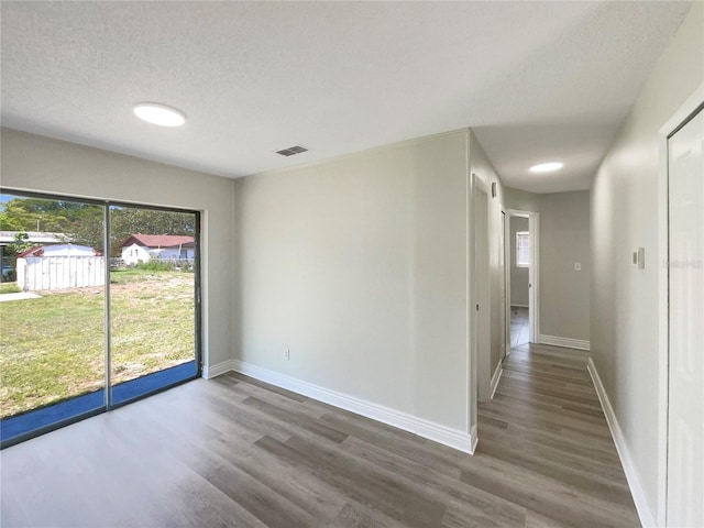 unfurnished room featuring healthy amount of natural light, wood finished floors, baseboards, and a textured ceiling