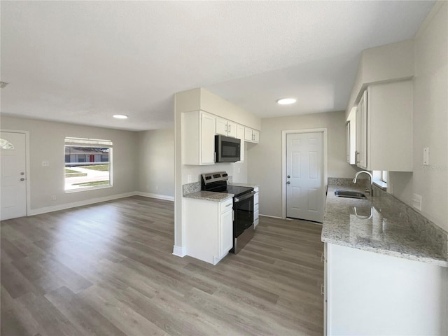 kitchen featuring appliances with stainless steel finishes, a sink, light wood-style flooring, light stone counters, and white cabinets