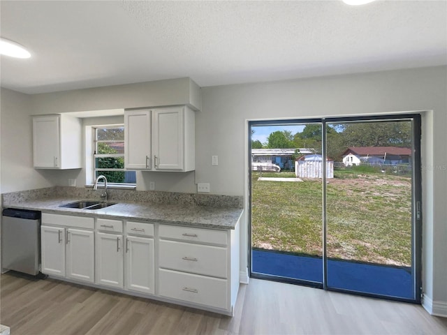 kitchen with dishwasher, a sink, light wood-style flooring, white cabinetry, and a textured ceiling