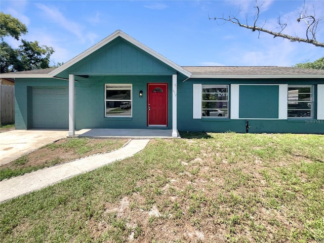 ranch-style home with a porch, a front yard, an attached garage, and driveway