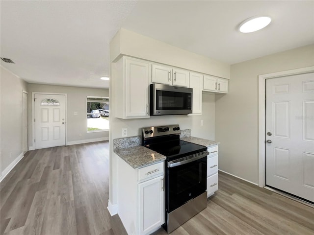 kitchen featuring stainless steel appliances, light stone counters, white cabinetry, light wood-type flooring, and baseboards