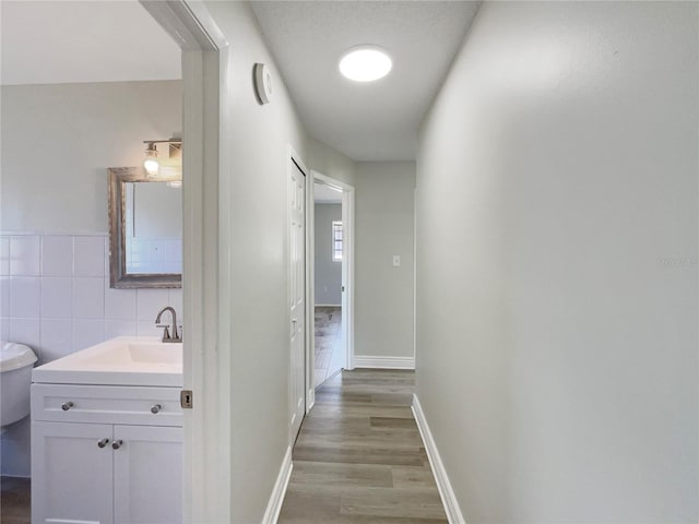 hall with wood finished floors, a sink, and tile walls