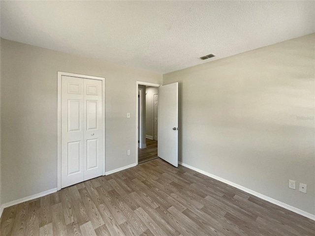 unfurnished bedroom featuring wood finished floors, baseboards, a textured ceiling, and a closet