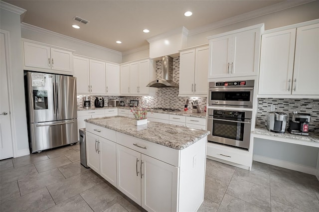kitchen with stainless steel appliances, wall chimney exhaust hood, ornamental molding, backsplash, and white cabinetry