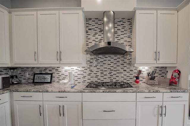 kitchen with wall chimney range hood, stainless steel gas stovetop, tasteful backsplash, and white cabinets