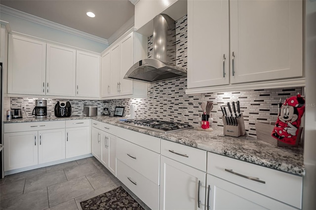 kitchen with wall chimney range hood, stainless steel gas stovetop, ornamental molding, white cabinetry, and tasteful backsplash