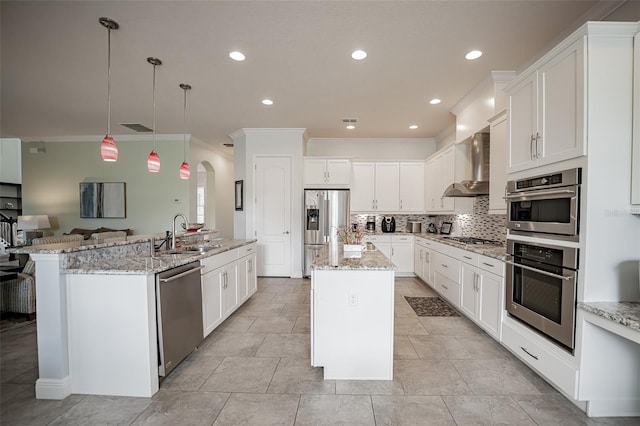 kitchen featuring a center island with sink, appliances with stainless steel finishes, a sink, wall chimney exhaust hood, and ornamental molding