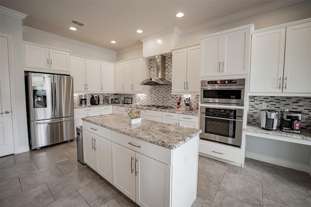 kitchen featuring appliances with stainless steel finishes, wall chimney exhaust hood, tasteful backsplash, a center island, and crown molding