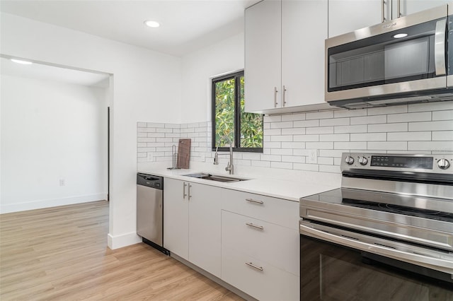 kitchen with stainless steel appliances, a sink, light countertops, light wood-style flooring, and baseboards