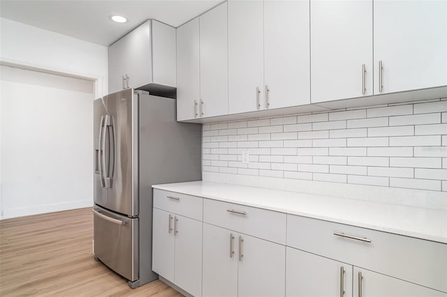 kitchen featuring light countertops, decorative backsplash, light wood-type flooring, baseboards, and recessed lighting