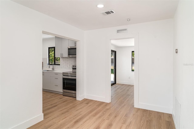 kitchen with appliances with stainless steel finishes, light wood-type flooring, tasteful backsplash, a sink, and recessed lighting