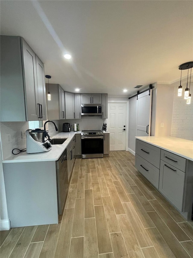 9153 86th Ave, Seminole, FL 33777 - kitchen featuring stainless steel appliances, gray cabinetry, a sink, a barn door, and light wood-style flooring
