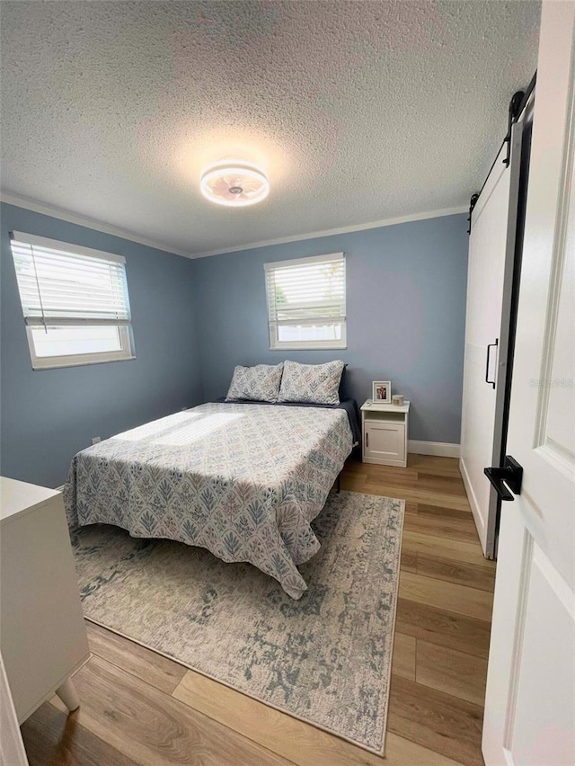 9153 86th Ave, Seminole, FL 33777 - bedroom with a barn door, light wood-style floors, multiple windows, a textured ceiling, and crown molding