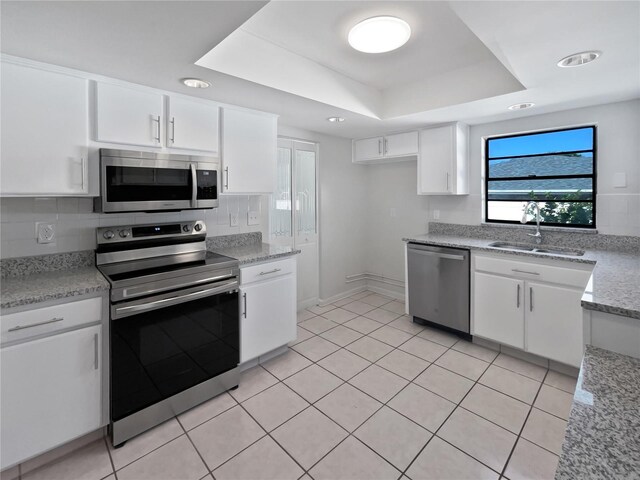 6623 Baybrooks Cir, Temple Terrace, FL 33617 - kitchen featuring stainless steel appliances, a tray ceiling, a sink, white cabinets, and light tile patterned flooring