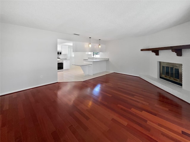6623 Baybrooks Cir, Temple Terrace, FL 33617 - unfurnished living room featuring light wood-type flooring, a glass covered fireplace, a textured ceiling, and baseboards