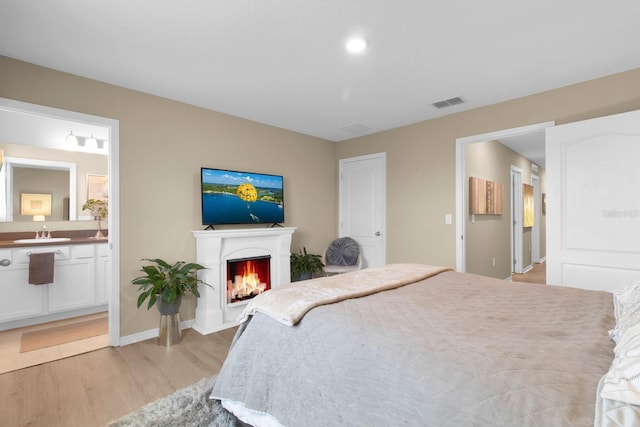 316 Primrose Dr, Davenport, FL 33837 - bedroom with light wood-style floors, a sink, a lit fireplace, connected bathroom, and baseboards