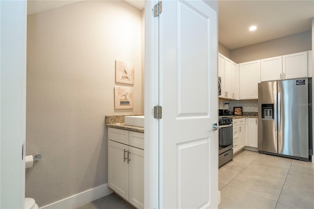 kitchen with stainless steel appliances, stone counters, white cabinetry, and light tile patterned floors