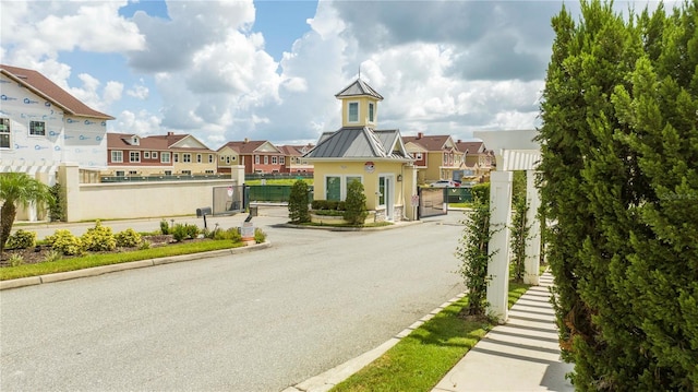 view of asphalt road featuring a residential view, curbs, and a gated entry