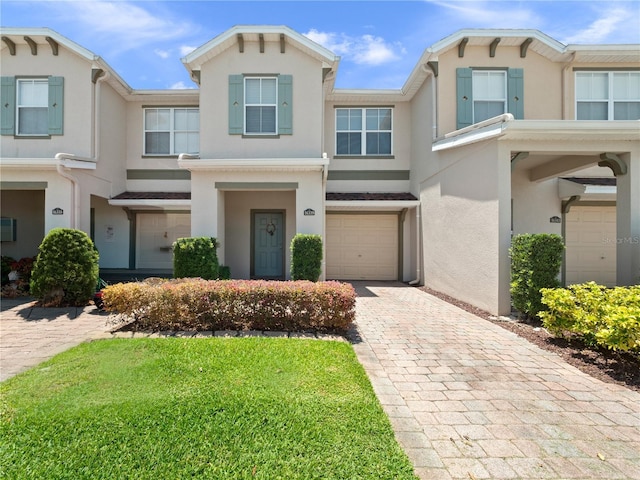 view of property with stucco siding, a garage, decorative driveway, and a front lawn