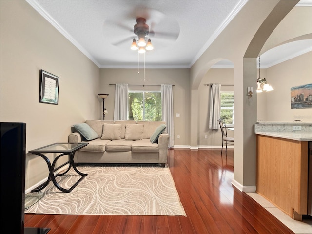 living room featuring arched walkways, ceiling fan, wood finished floors, crown molding, and baseboards