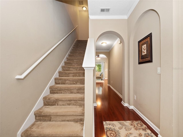 stairway with crown molding, arched walkways, wood finished floors, and baseboards