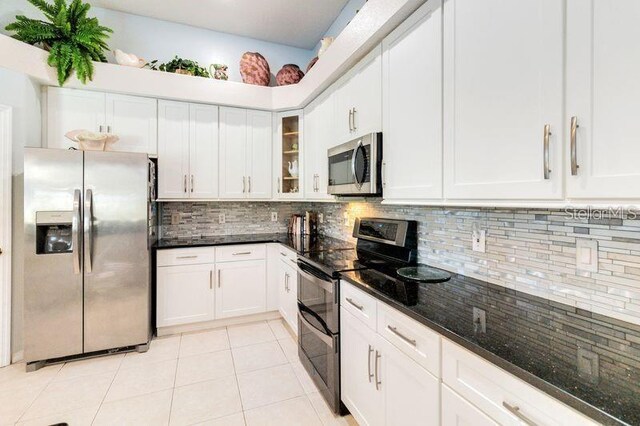 10642 Cloudview Dr, Orlando, FL 32825 - kitchen with stainless steel appliances, backsplash, dark stone counters, light tile patterned floors, and white cabinets