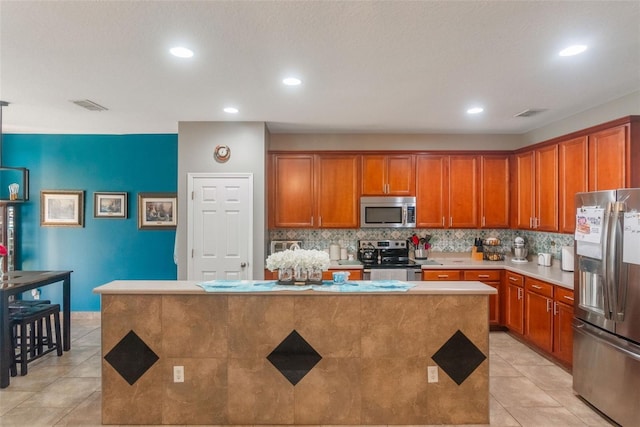 2619 Breezy Meadow Rd, Apopka, FL 32712 - kitchen featuring stainless steel appliances, brown cabinets, light tile patterned floors, a kitchen island, and decorative backsplash