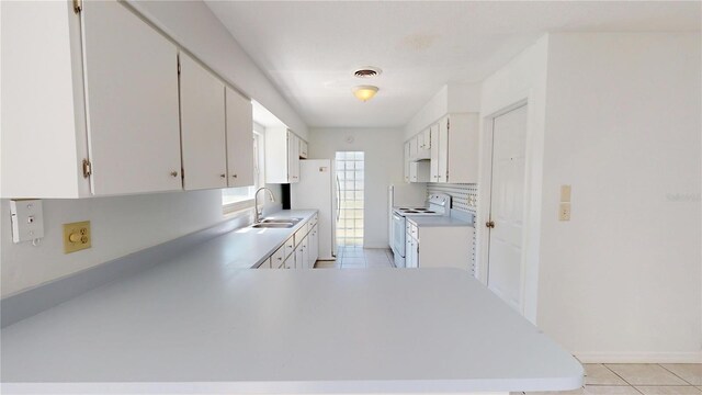 1119 Edith Dr, Daytona Beach, FL 32117 - kitchen with white appliances, light countertops, light tile patterned floors, white cabinets, and a peninsula