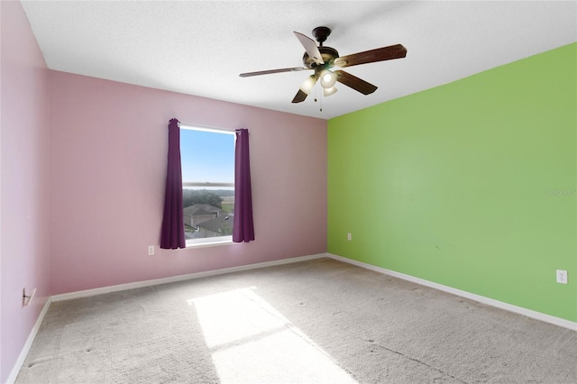 carpeted spare room featuring ceiling fan and baseboards