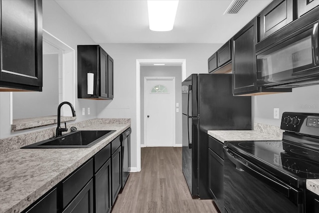 2357 E Dana Dr, Deltona, FL 32738 - kitchen with black appliances, a sink, light wood finished floors, dark cabinetry, and light countertops