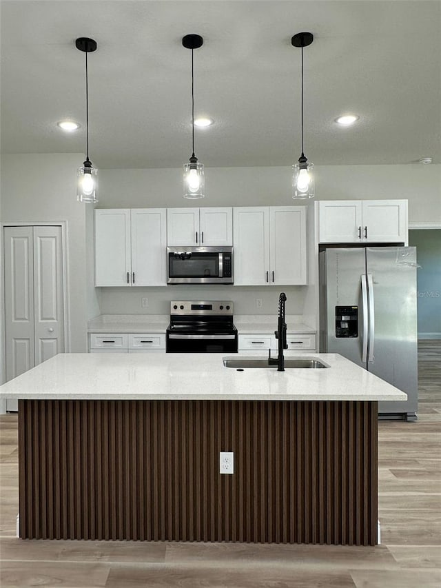 3063 SW 168th Loop, Ocala, FL 34473 - kitchen with stainless steel appliances, a sink, light wood-type flooring, a kitchen island with sink, and white cabinetry