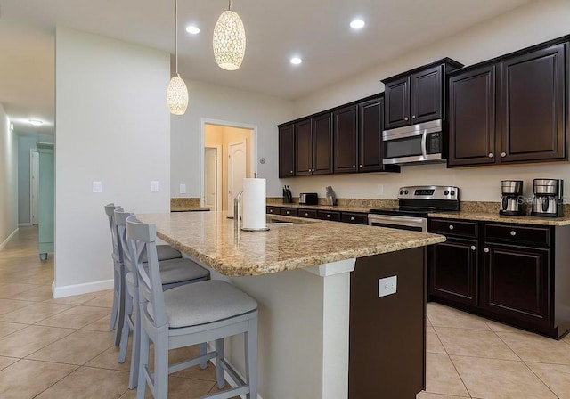 kitchen featuring appliances with stainless steel finishes, light tile patterned floors, a kitchen island with sink, a breakfast bar, and pendant lighting