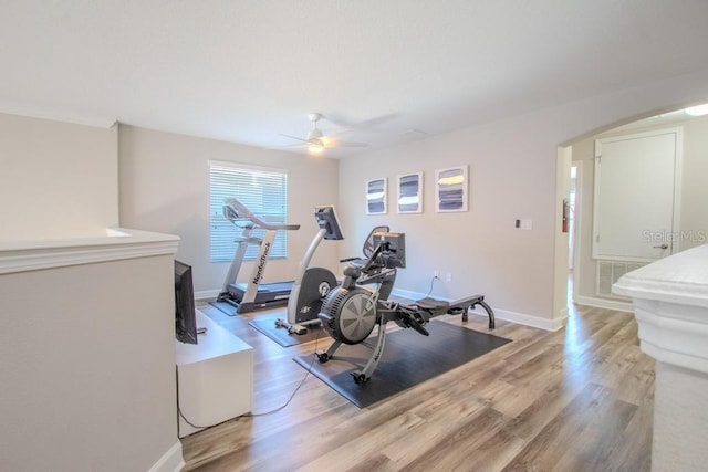 workout room with a ceiling fan, arched walkways, light wood-style floors, and baseboards