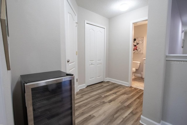 corridor featuring beverage cooler, wood finished floors, and baseboards