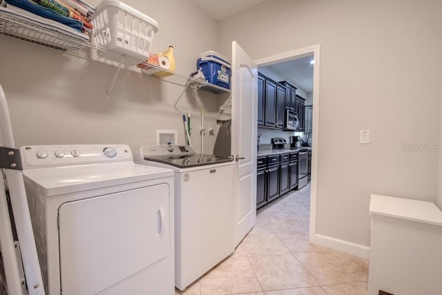 washroom featuring washing machine and dryer, light tile patterned flooring, and baseboards