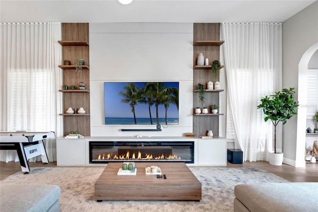 15947 Vetta Dr, Bella Collina, FL 34756 - living room featuring a glass covered fireplace, healthy amount of natural light, arched walkways, and wood finished floors