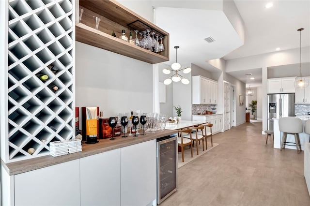 15947 Vetta Dr, Bella Collina, FL 34756 - indoor dry bar featuring wine cooler, tasteful backsplash, pendant lighting, recessed lighting, and stainless steel fridge with ice dispenser