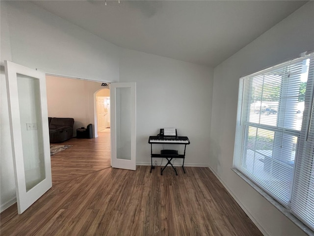 unfurnished room featuring vaulted ceiling, arched walkways, dark wood-type flooring, and baseboards