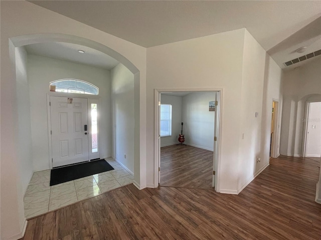 foyer entrance with arched walkways, baseboards, and wood finished floors