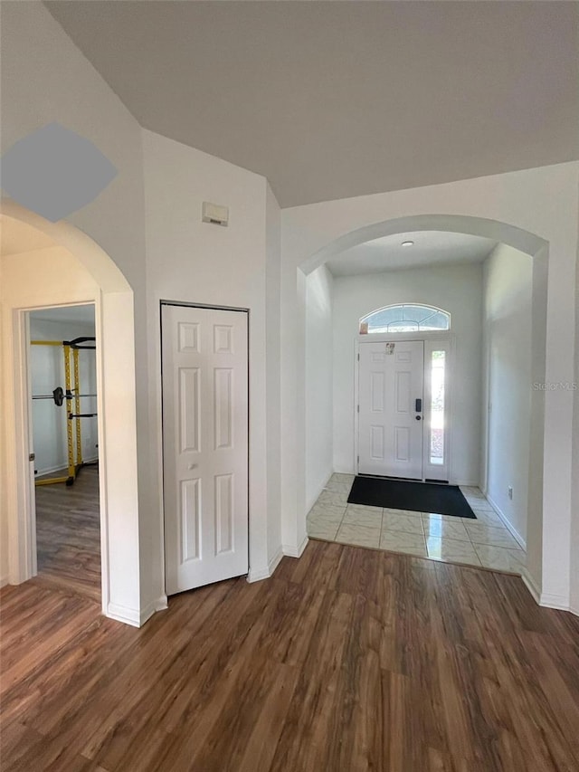 foyer featuring wood finished floors, baseboards, arched walkways, and vaulted ceiling