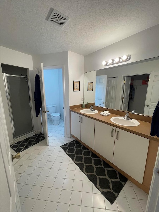 bathroom featuring a shower stall, tile patterned flooring, double vanity, toilet, and a textured ceiling