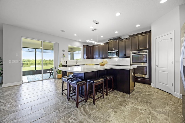 15208 Lake Claire Overlook Dr, Winter Garden, FL 34787 - kitchen with stainless steel appliances, light countertops, a kitchen island, dark brown cabinets, and a kitchen breakfast bar