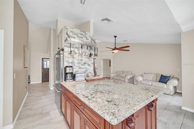 kitchen with ceiling fan, baseboards, light stone counters, brown cabinets, and open floor plan