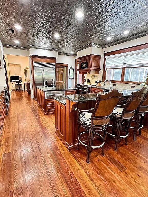 11317 NW 199th Ave, Alachua, FL 32615 - kitchen featuring an ornate ceiling, light wood-style floors, an island with sink, a breakfast bar area, and built in refrigerator